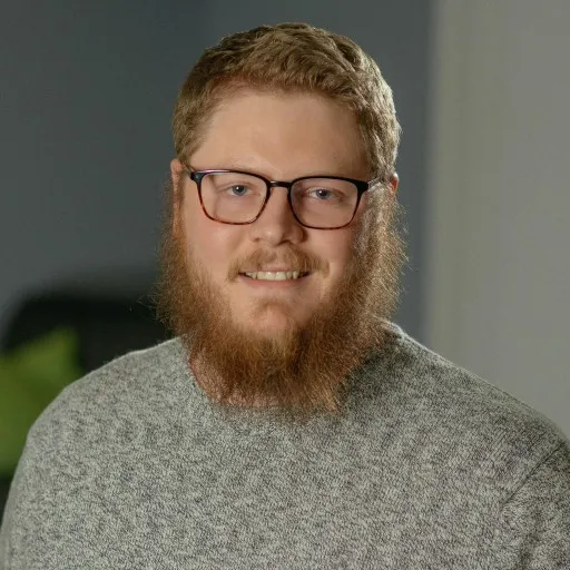 Red haired man with beard and glasses smiling